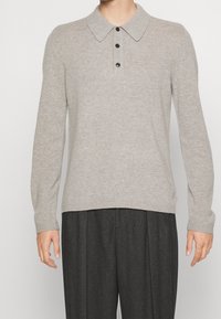 Pullover lavorato a maglia grigio chiaro con colletto, cinque bottoni neri e maniche lunghe. Presenta una texture a costine e una vestibilità morbida.