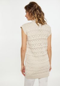 Beige gebreide mouwloze top met een textuurpatroon van horizontale lijnen en openwork ontwerpen, afgewerkt met een ribbelzoom.