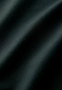 Tissu noir affichant une texture lisse avec un léger brillant, présentant des plis doux qui créent des vagues délicates et une apparence en profondeur.