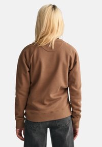 Brązowa bluza z okrągłym dekoltem, raglanowymi rękawami oraz ściągaczami u mankietów i na dole. Miękka tkanina, luźny krój i bezszwowy design pleców.