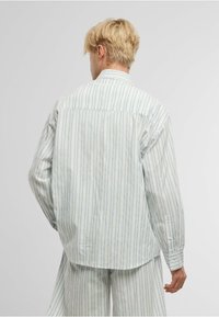 Camisa de manga larga a rayas azul claro y blanca con un corte relajado, puños abotonados y un dobladillo redondeado. Fabricada en algodón suave y texturizado.