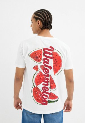 Camiseta blanca de algodón que presenta un gráfico colorido de sandía en la parte posterior, con letras rojas que dicen "Sandía" y varios diseños de rodajas de sandía.