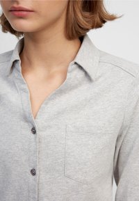 Gray button-up shirt made of soft fabric. Features a collar and a chest pocket, with dark buttons on the front. Simple, clean design.