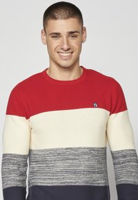 Maglione a maglia con righe orizzontali rosse, crema e navy. Texture a coste con un piccolo logo sul lato sinistro del petto. Collo rotondo.