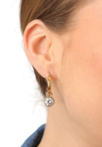 Gouden creolen met een ronde heldere edelsteen hanger, met een glanzende afwerking en een gladde textuur, gedragen aan de oorlel.
