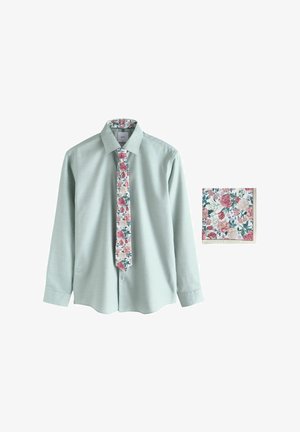 Cămașă verde deschis cu mâneci lungi, cravată cu model floral și batistă de buzunar asortată pe fundal alb.