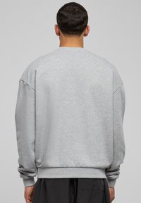 Sudadera gris de cuello redondo con hombros caídos, puños y dobladillo de canalé, fabricada en una suave mezcla de algodón. La vista trasera no presenta gráficos ni logotipos.
