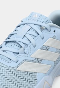 Zapatilla deportiva azul clara con parte superior de malla, detalles texturizados y tres rayas blancas. Los cordones son planos y la lengüeta incluye la marca.