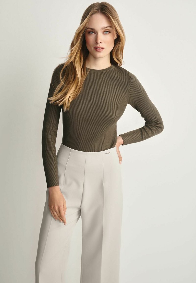 Prążkowany oliwkowozielony top z długim rękawem w połączeniu z jasnymi beżowymi spodniami z wysokim stanem, charakteryzującymi się prostą sylwetką i subtelnym logo marki.