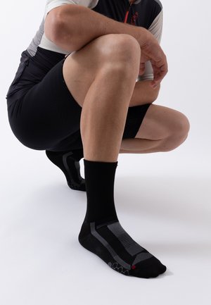 Male cyclist crouching, wearing black compression socks with gray accents and black cycling shorts against a white background.
