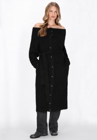 Cardigan lung negru, fără umeri, realizat dintr-un material tricotat texturat. Dispune de nasturi în față și o curea asortată. Buzunare vizibile.