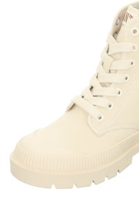 Canvas ankle boot in cream, featuring a textured rubber sole, round toe, and traditional lace-up design with metal eyelets.