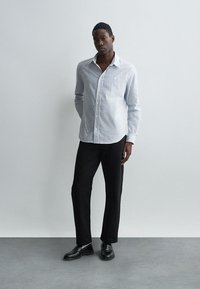 Dryžuota balta ir tamsiai mėlyna marškinėlių palaidinė su ilgomis rankovėmis, derinama su juodomis kelnėmis ir juodais batais. Paprastas dizainas, prigludusi forma.