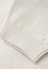 Pull en tricot blanc avec un ourlet côtelé et une texture lisse, mettant en avant son design simple et son tissu doux.