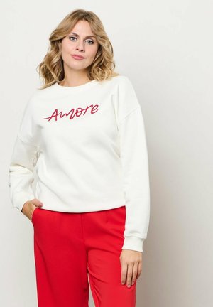 Witte sweatshirt met rode "Amore" borduring, ontspannen pasvorm, geribbelde manchetten, gecombineerd met rode broek. Zachte textuur, casual ontwerp.