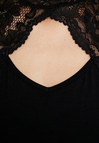 Schwarzes Oberteil mit einem Spitzen-Ausschnitt, floralen Mustern, gewellten Kanten und einem tiefen V-förmigen Ausschnitt im Brustbereich.