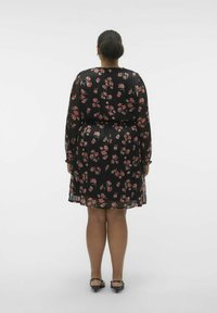 Robe plissée noire avec de longues manches transparentes, ornée de motifs floraux roses, cintrée à la taille et associée à des sandales à talons noires.