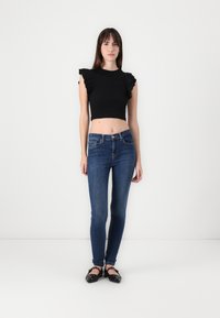Black cropped top with ruffled sleeves, paired with fitted blue denim jeans. The outfit is completed with black flats featuring decorative hardware.