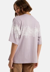 Lavendel T-shirt met korte mouwen en een bloemenpatroon in het wit op de achterkant. Zachte katoenen stof, ontspannen pasvorm, ronde hals en rechte zoom.