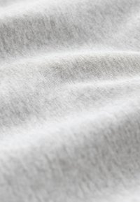 Zbliżenie na miękką, jasnoszarą tkaninę o delikatnej fakturze dzianiny z łagodnymi fałdami tworzącymi subtelne cienie i refleksy świetlne.