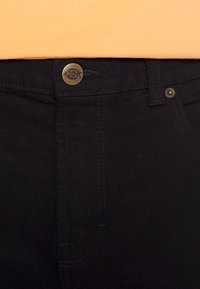 Vaqueros de mezclilla negros con cierre de botón dorado, costuras en contraste y un diseño de corte slim. La tela tiene una textura suave.