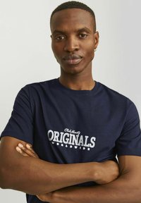 Camiseta de algodón azul marino con estampado blanco "Club Ninety Originals Worldwide". Manga corta, cuello redondo, diseño ajustado. Textura suave.