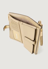 Portafoglio in pelle beige con più slot per carte, un comparto con zip e una chiusura a strap frontale. Accenti in hardware dorato. Texture liscia.