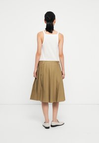 Gonna kaki plissettata con vita aderente, abbinata a una canotta bianca, vista da dietro. Il materiale appare liscio con un design strutturato.