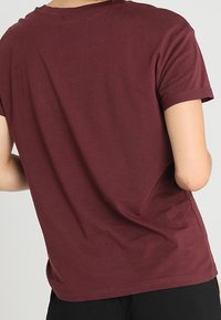 Camiseta de manga corta color burdeos, con cuello redondo, material de algodón suave, corte relajado, textura lisa, con puños de manga enrollados y sin gráficos visibles.