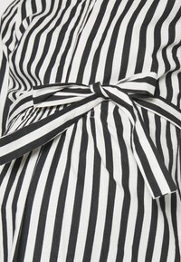 Svart och vit vertikalt randig kläde med en knytning i midjan och mjuk textur, med veck för extra struktur.