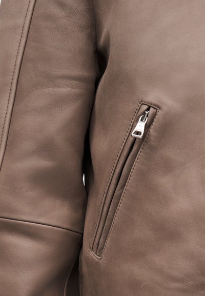 Κοντινή λήψη στο μπουφάν από δέρμα σε απόχρωση ταουπ, που δείχνει λεπτομερή ραφή και μια μικρή κάθετη τσέπη με φερμουάρ και ασημένιο έλκηθρο.