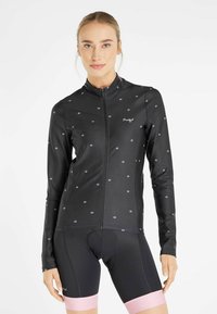 Black cycling jacket with small white flower patterns, long sleeves, full zipper, and a fitted design. Worn over black shorts with pink accents.