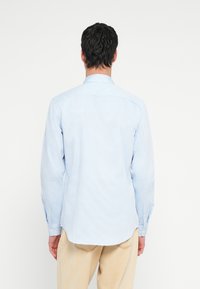 Camisa de manga comprida às riscas azul claro com gola com botões, bainha reta e botões nos punhos, feita de tecido leve.