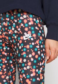 Nike leggings med en svart bakgrund och ett färgglatt blommönster i rosa, vitt och blått, med en vit Nike-logga på låret.