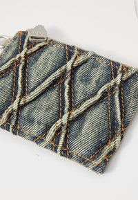 Denim wallet featuring a quilted pattern with diagonal stitching in orange. Accompanied by a silver zipper pull for closure.