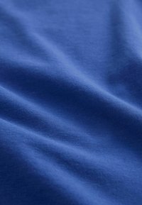 Tessuto di cotone blu con una texture liscia, caratterizzato da pieghe e grinze sottili. Il materiale ha un colore uniforme senza motivi o accenti.