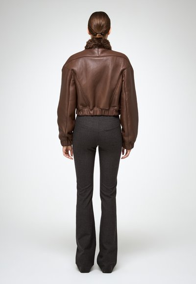 Bruine leren cropped jas met een bontkraag, elastische taille en opgezette mouwen, gecombineerd met grijze flared broeken. Achteraanzicht.