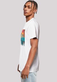Witte katoenen t-shirt met een kleurrijke bergafbeelding op de voorkant, met blauwe en oranje tinten, en een ontspannen pasvorm.