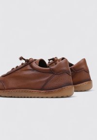 Zapatos de cuero marrón con un acabado texturizado, forma redondeada y suela flexible; cuentan con un diseño de cordones y acentos de costura decorativa.