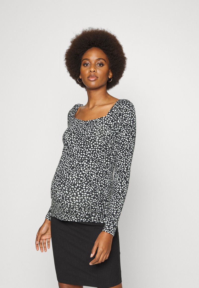 Camisola preta de manga longa com padrão de manchas brancas, decote quadrado e tecido elástico, combinada com uma saia preta canelada.