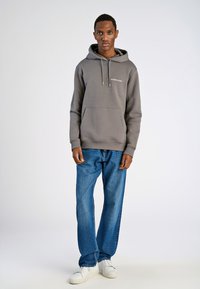 Grijze hoodie met een voorzak, trekkoorden en merklogo. Draag met blauwe jeans en witte sneakers. Eenvoudig, casual ontwerp.