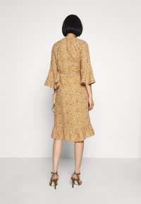 Vestido envolvente floral en color mostaza, con mangas acampanadas de tres cuartos y un dobladillo con volantes. Tejido ligero con una textura suave.