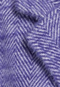 Fialový textil v rybí kostce s měkkou, chlupatou texturou a bílými akcenty. Vzor je šikmý s ostrými ševronovými tvary.