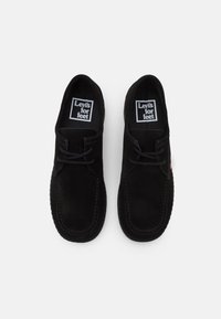Pár černých semišových volnočasových šněrovacích bot viděných z vrchu, s označením „Levi's for feet“ uvnitř každé boty.