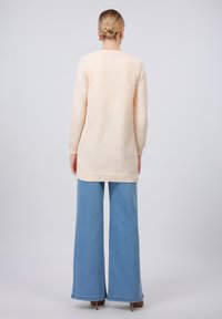 Sweater em marfim com uma textura suave, mangas longas e uma bainha traseira em forma de cavalo, combinado com jeans de perna larga azul claro.