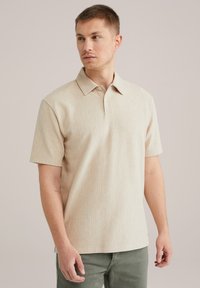 Bež kratkosleeve polo majica z teksturiranim rebrastim vzorcem in s koničastim ovratnikom, ki ima tri gumbe na vratu in sproščen kroj.