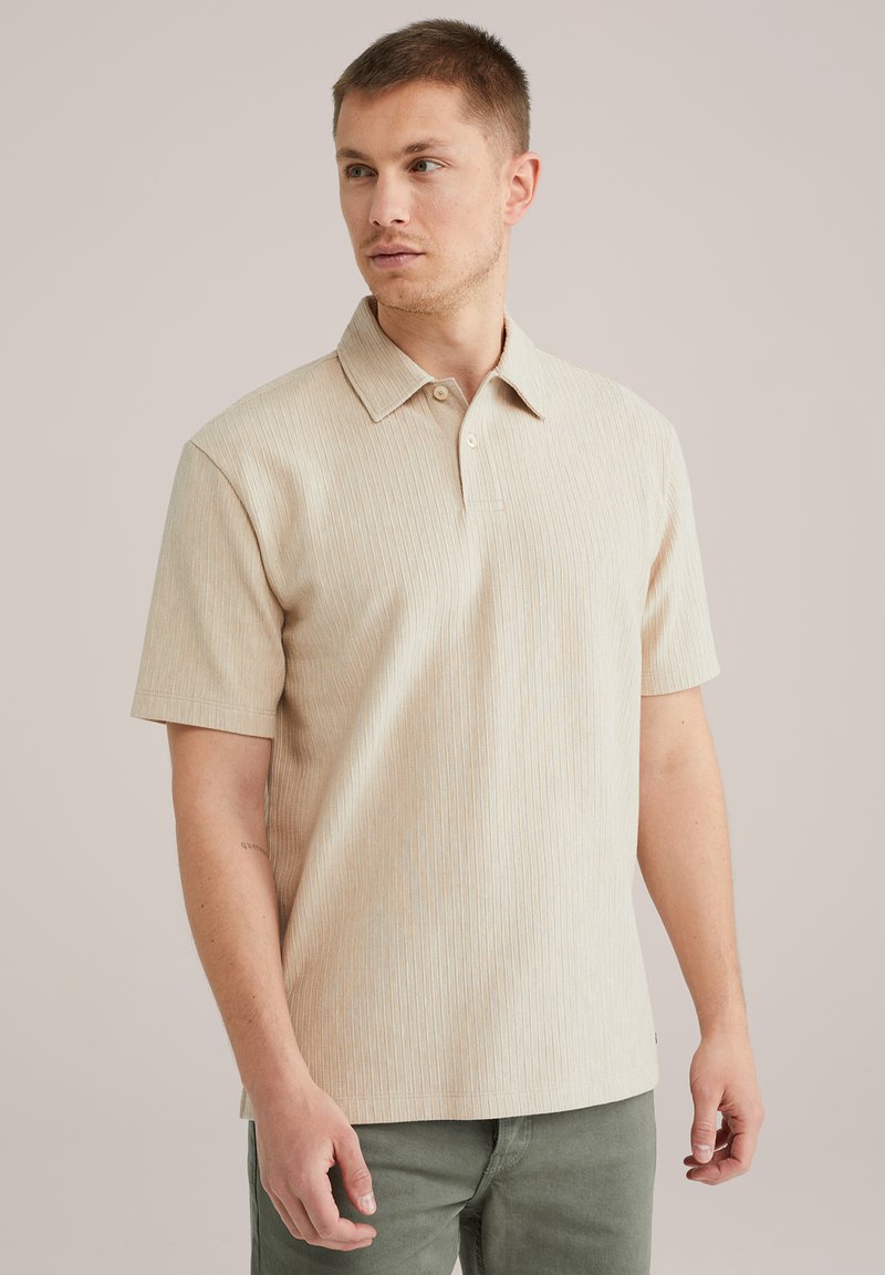 Bež kratkosleeve polo majica z teksturiranim rebrastim vzorcem in s koničastim ovratnikom, ki ima tri gumbe na vratu in sproščen kroj.