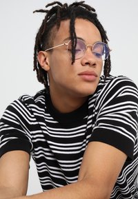 Haut en tricot noir et blanc à rayures, à manches courtes et col rond. Lunettes rondes avec des montures métalliques fines et des verres clairs.