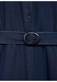 Robe en denim bleu foncé avec une large ceinture dotée d'une grande boucle noire ovale et un devant boutonné.