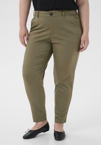 Olijfgroene op maat gemaakte broek met een medium taille, rechte pijpen, zijzakken en een enkele knoopsluiting. Gekaapt met zwarte platte schoenen.